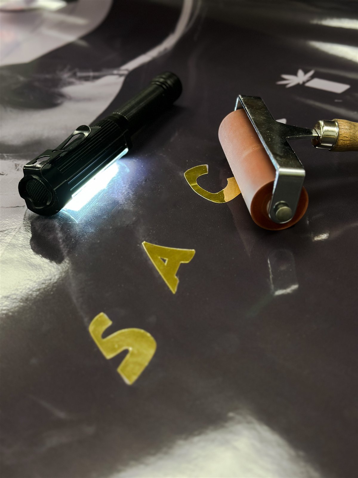 Roller applying layered gold mirror vinyl lettering to the wrap