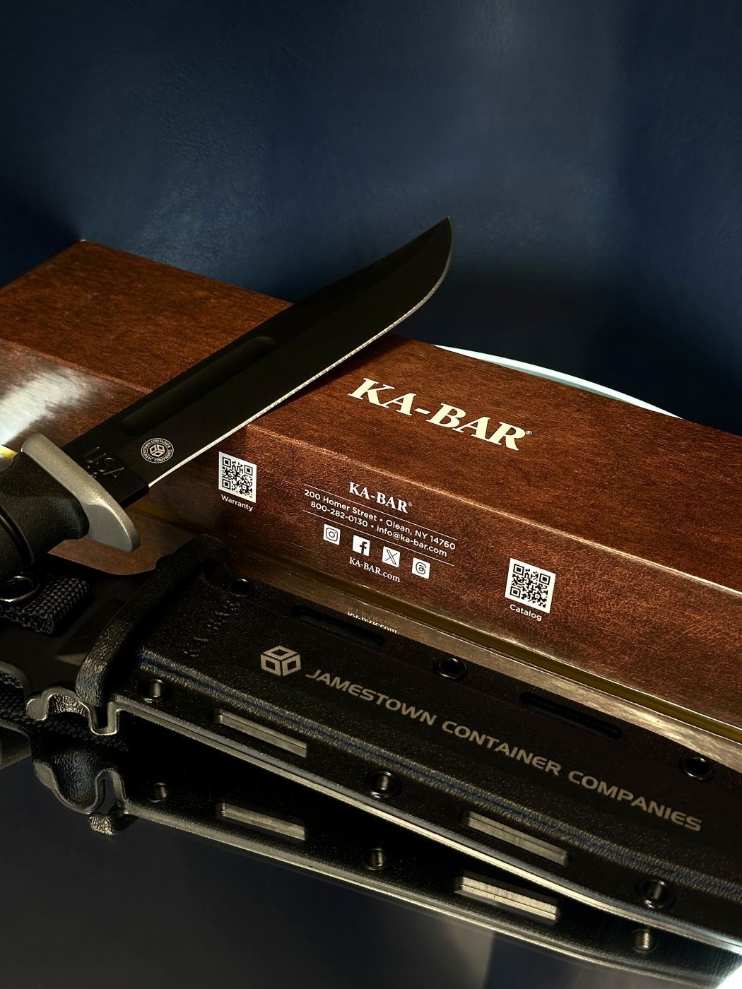 KA-BAR knife resting on its wooden box with the Jamestown Container Companies laser-engraved sheath below